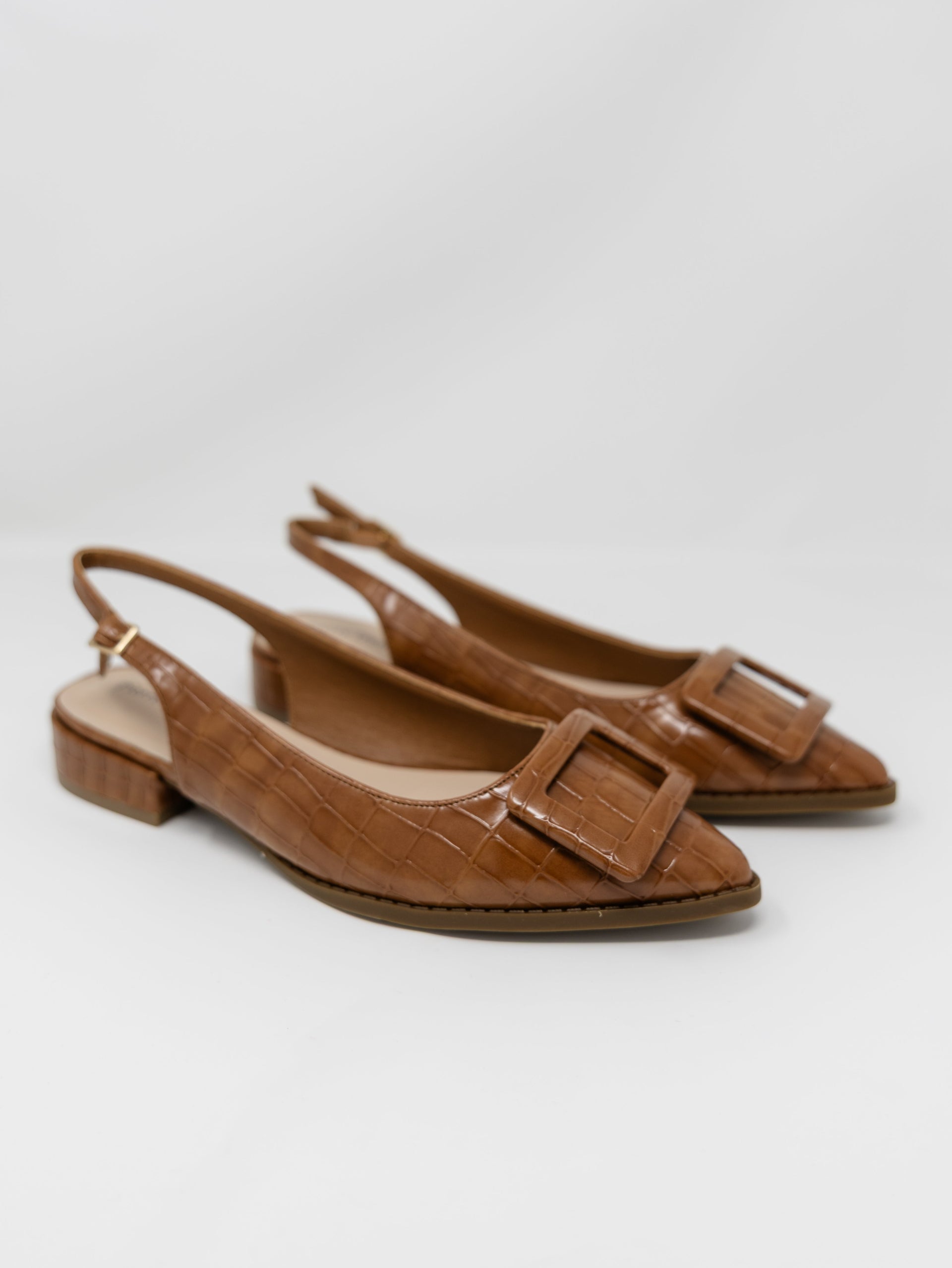 A pair of Pierre Dumas brown croc-embossed pointed-toe slingback flats displayed against a solid white background. The shoes feature an adjustable ankle strap with a small gold buckle, a low block heel, and a large matching brown square buckle detail across the toe box.