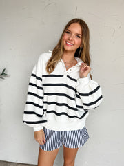 White pullover with black horizontal stripes, a collared snap neckline, dropped shoulders, long sleeves, and ribbed cuffs and hem, made of 55% polyester and 45% cotton.