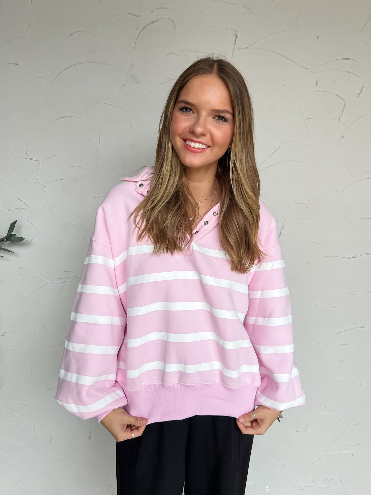 Light pink pullover with white horizontal stripes, a collared snap neckline, dropped shoulders, long sleeves, and banded cuffs and hem, made of 55% polyester and 45% cotton.