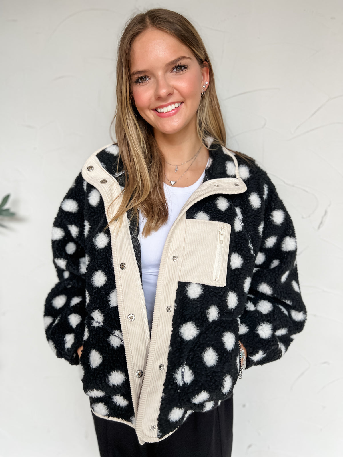 Black fleece jacket with off-white polka dots, contrasting off-white trim, snap-front closure, zippered pockets, and an oversized fit, made of 100% polyester.
