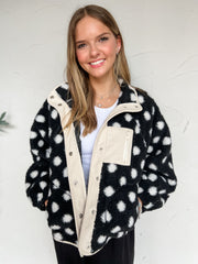 Black fleece jacket with off-white polka dots, contrasting off-white trim, snap-front closure, zippered pockets, and an oversized fit, made of 100% polyester.
