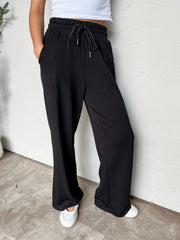 Black wide-leg pants with an elastic drawstring waistband, side pockets, and front seam detailing, made of 47% rayon, 46% polyester, and 7% spandex.