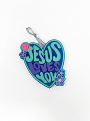 This "Jesus Loves You" car freshie features a groovy, heart-shaped design with retro lettering, accented by a tiny smiley face and small flower details along the border. It comes ready to hang from your rearview mirror with an attached hanging hook. Colors and scents vary.