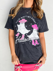 Catie wearing the black Lane Seven 100% cotton This Ain’t My First Halloween tee in size Medium, featuring white ghosts in pink cowboy hats and boots, star accents, and distressed-look lettering, styled with a pink mini skirt with sparkling bow details.