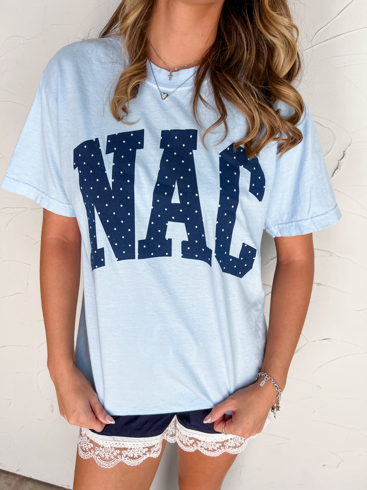 Catie wearing the Nac Polka Dot light blue Comfort Colors 100% ring-spun cotton tee in size Small, featuring large navy NAC lettering with white polka dots, a crew neckline, and short sleeves, styled with navy lace-trim drawstring shorts.⠋
