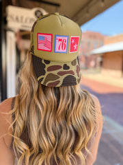 Person wearing a green and camouflage cap with patches outdoors