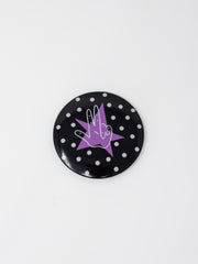 A round pin button featuring a black background with white polka dots, centered with a purple star and a white-outlined "Axe 'Em" hand gesture, displayed against a plain white background.