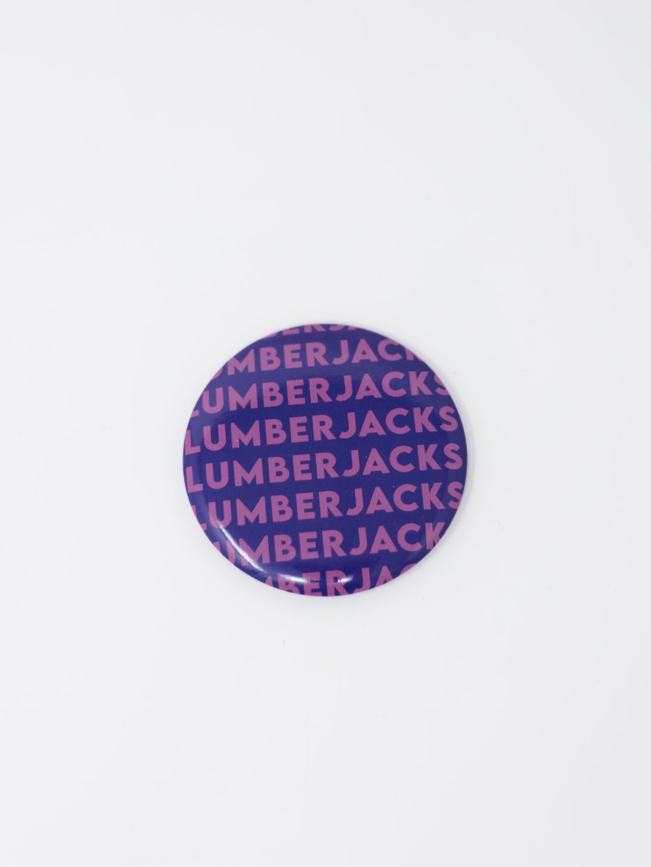 A round button badge featuring a purple and pink repeating pattern of the brand name 'LUMBERJACKS' on a plain white background.