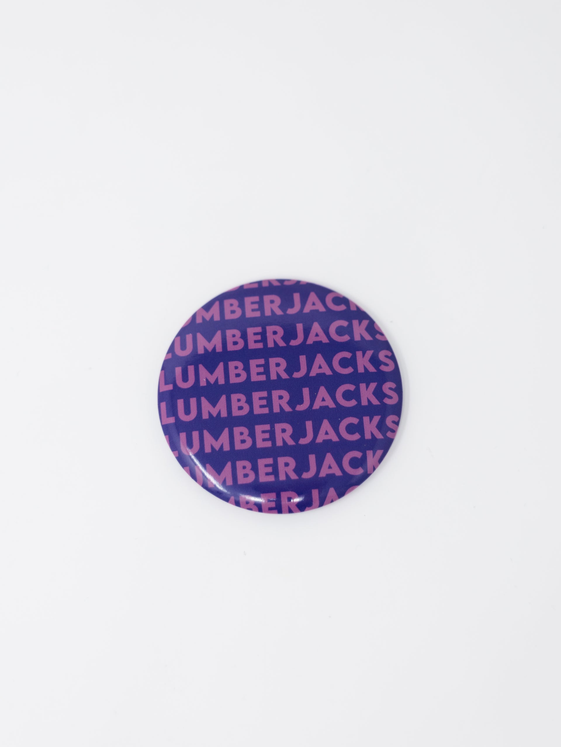 A round button badge featuring a purple and pink repeating pattern of the brand name 'LUMBERJACKS' on a plain white background.