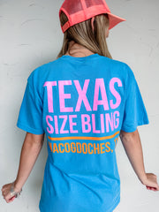 Person wearing a blue t-shirt with 'TEXAS SIZE BLING MACOGDOCHES' text, standing against a white wall.