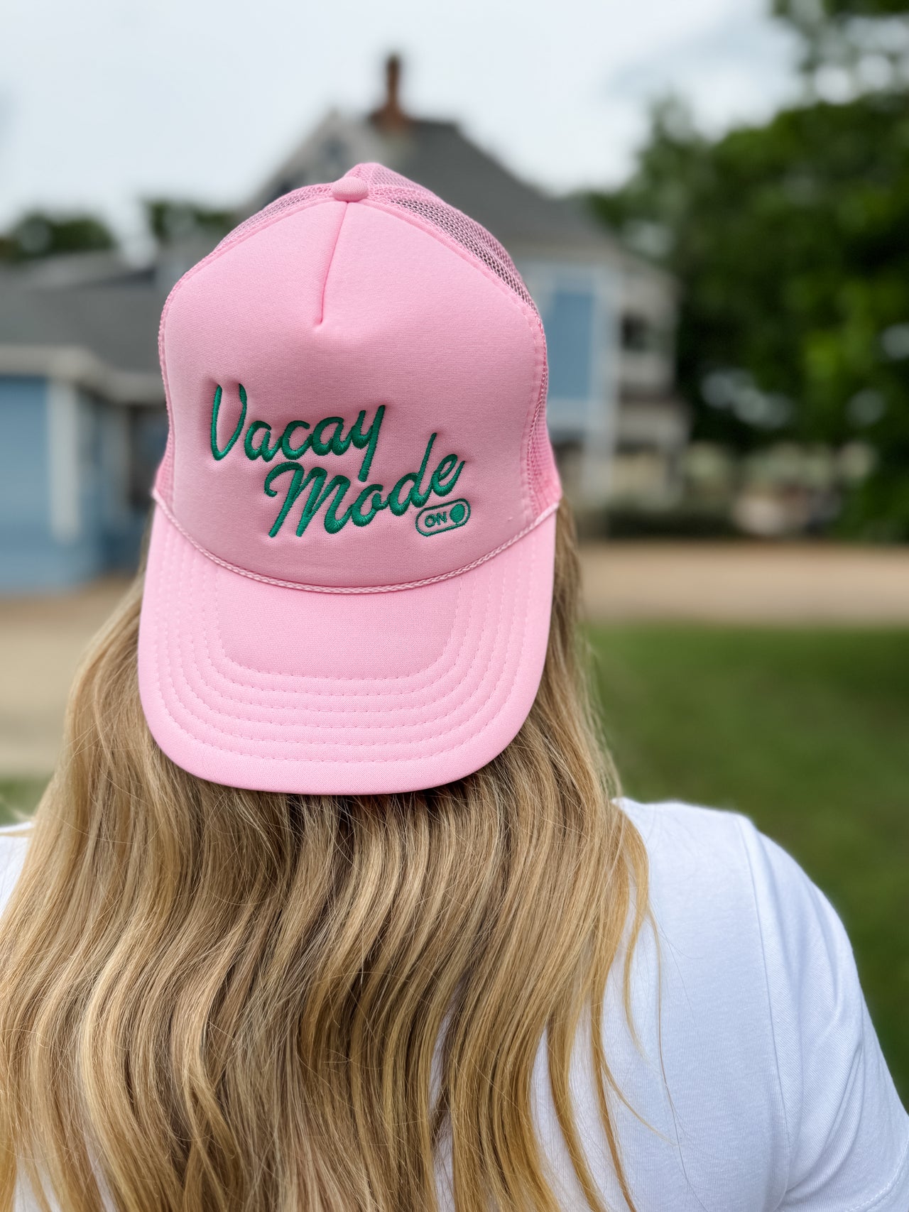 Person wearing a pink cap with 'Vacay Mode On' text outdoors.