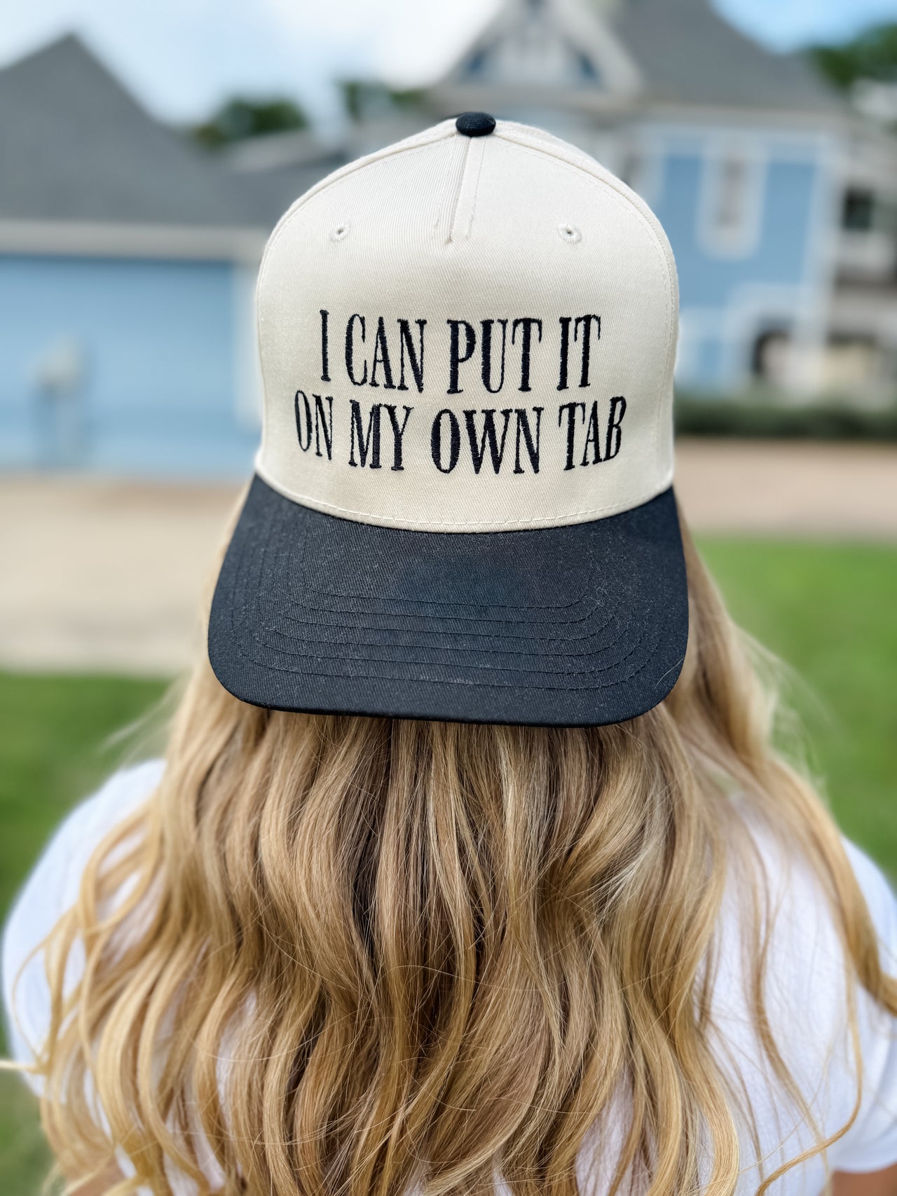 Person wearing a cap with text 'I can put it on my own tab' outdoors.