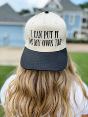 Person wearing a cap with text 'I can put it on my own tab' outdoors.