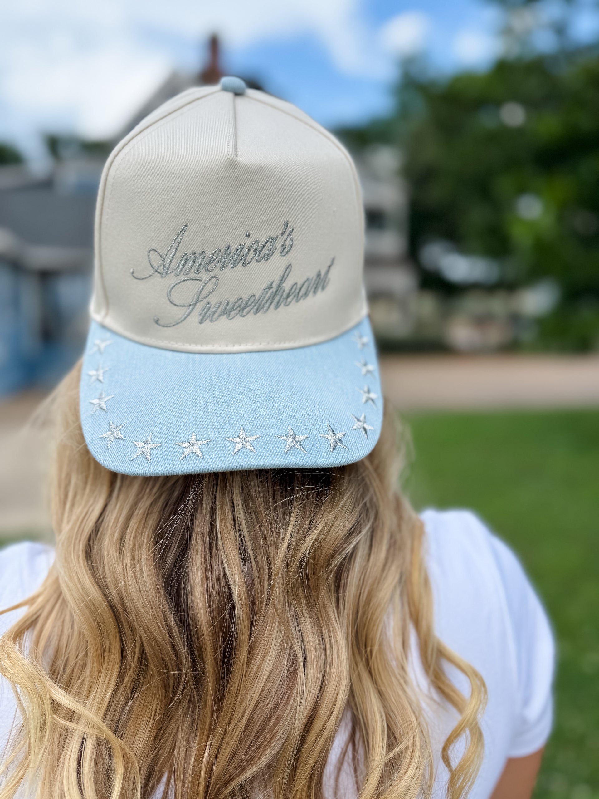 Person wearing a cap with 'America's Sweetheart' text and star details outdoors.