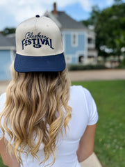 Person wearing a 'Blueberry Festival' cap with a blurred background of a house and trees.