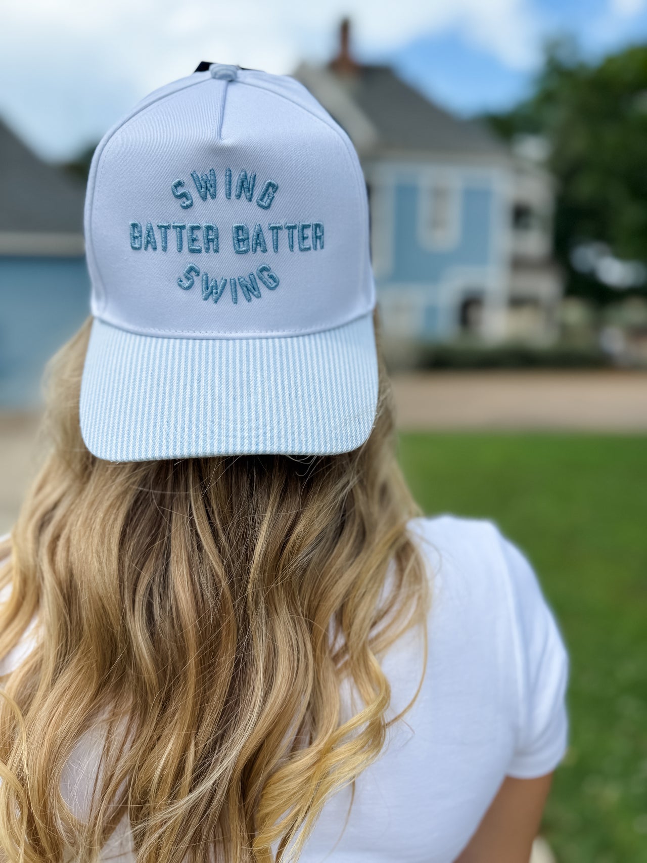 Person wearing a light blue cap with 'Swing Batter Batter Swing' text, standing outdoors.