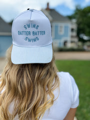 Person wearing a light blue cap with 'Swing Batter Batter Swing' text, standing outdoors.