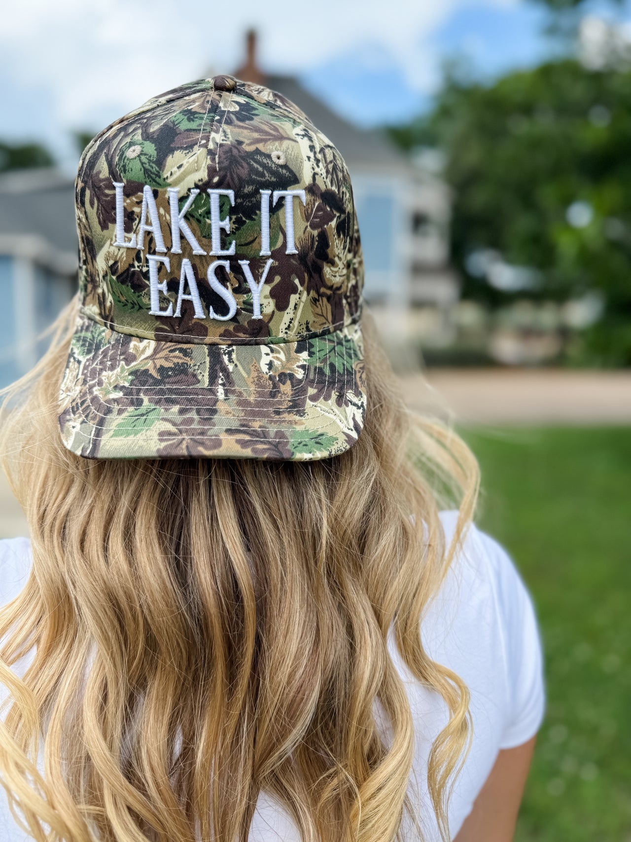 Person wearing a camouflage cap with 'Lake It Easy' text, outdoors.