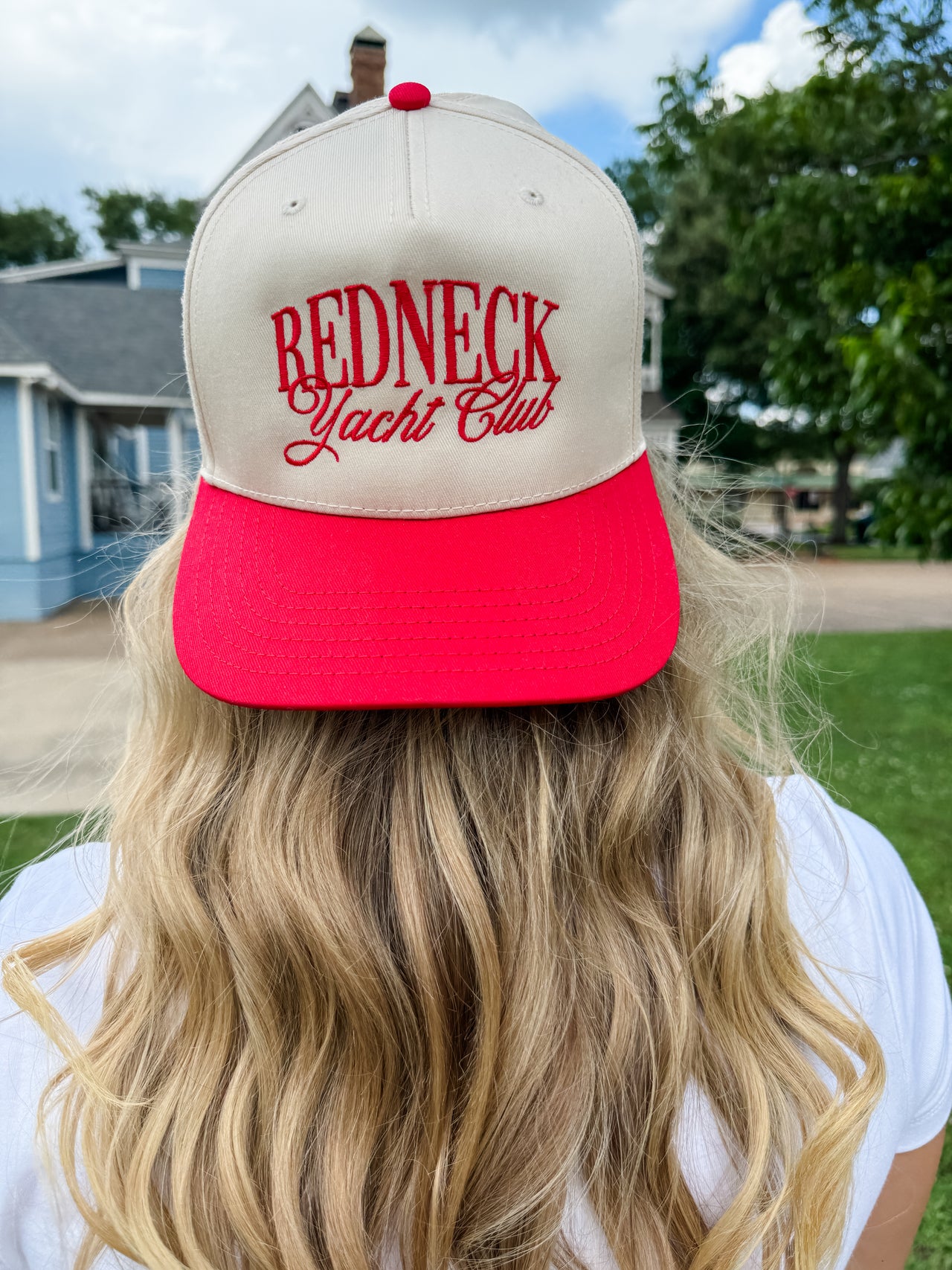 Person wearing a beige and red cap with 'Redneck Yacht Club' text outdoors.