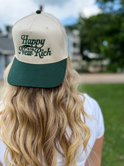 Person wearing a cap with 'Happy is the New Rich' text outdoors