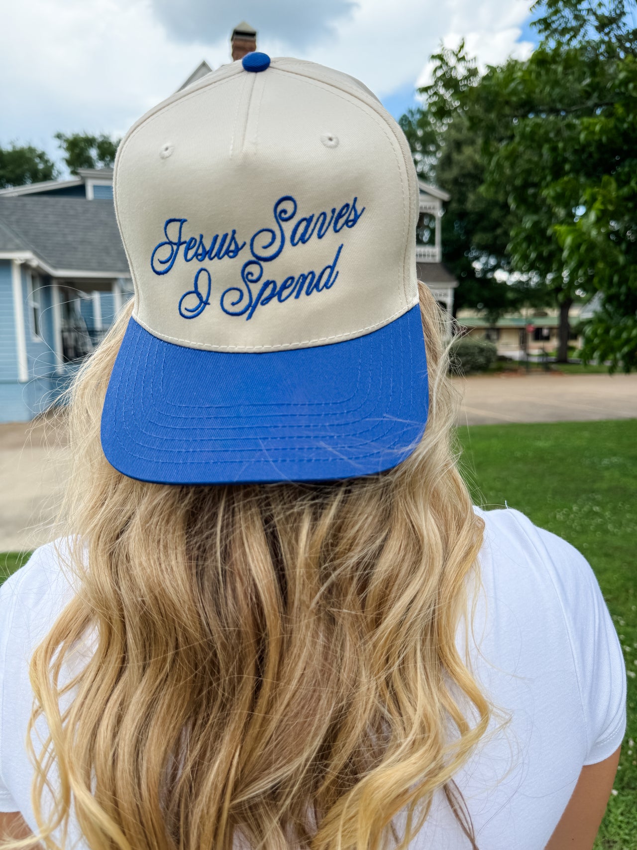 Person wearing a cap with 'Jesus Saves I Spend' text outdoors.