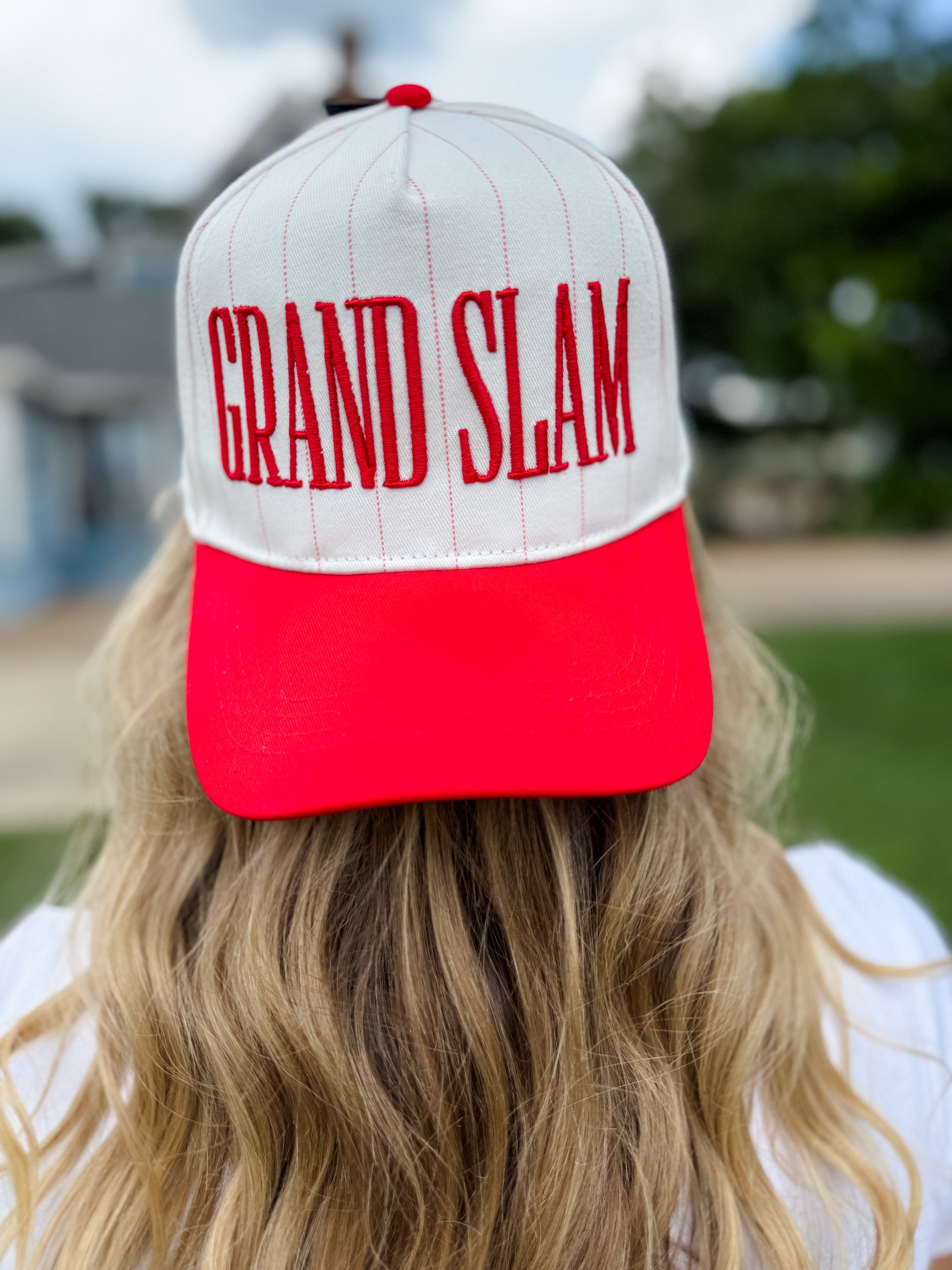 Person wearing a red and white cap with 'GRAND SLAM' text outdoors.