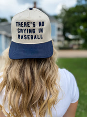 Person wearing a cap with 'There's no crying in baseball' text, blurred outdoor background