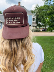 Person wearing a maroon cap with text, standing outdoors with a house and trees in the background