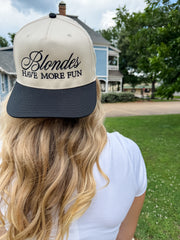 Person wearing a cap with 'Blondes Have More Fun' text outdoors.