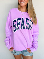 A woman wearing a 100% cotton lavender purple sweatshirt with 'SFASD' printed across the chest in navy blue letters with white dots, paired with denim shorts.