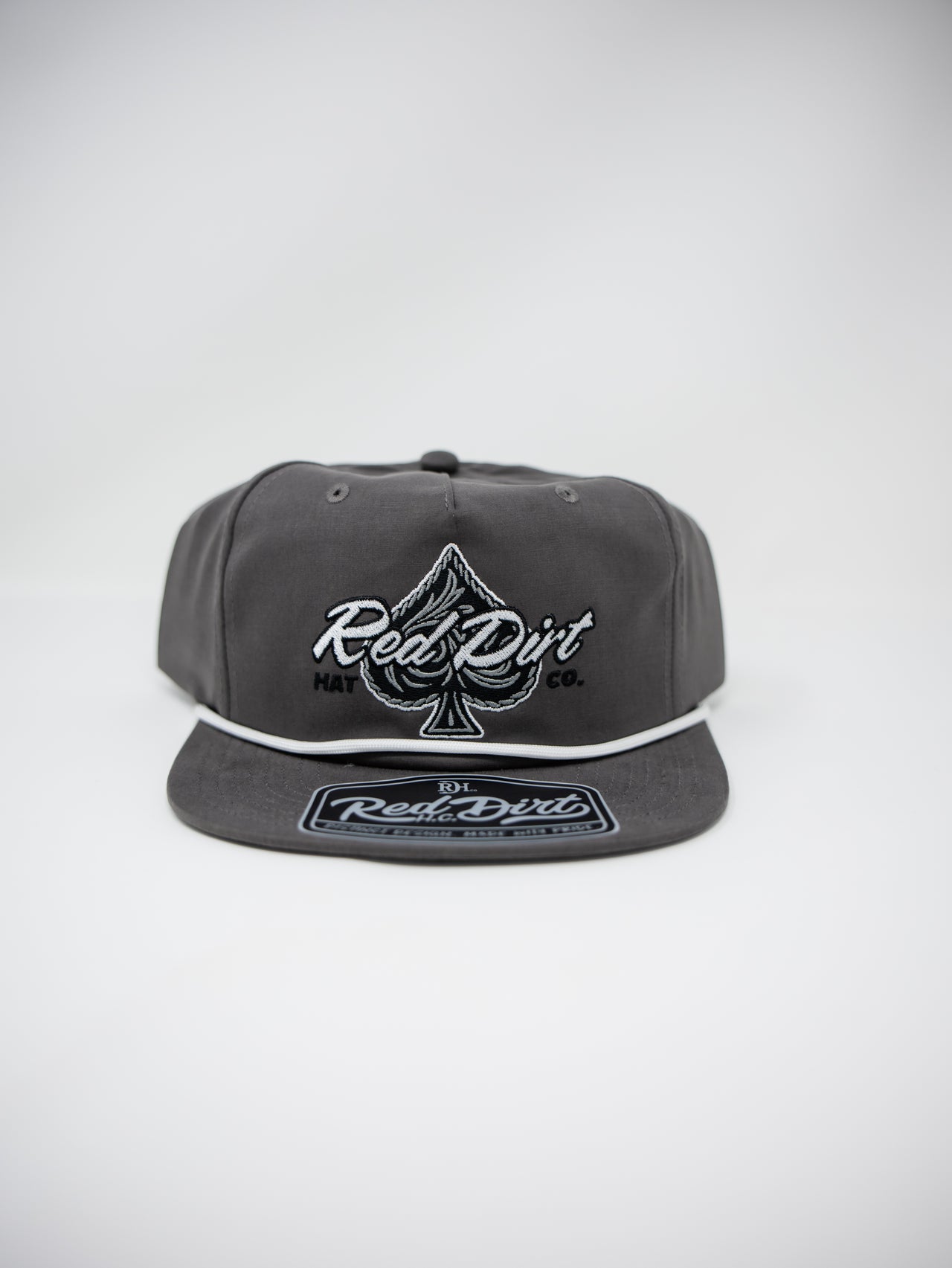 A dark gray snapback cap featuring a white embroidered Red Dirt logo and an ace of spades symbol on the front, with a matching Red Dirt patch on the flat visor, set against a light gray background.