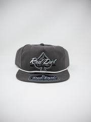 A dark gray snapback cap featuring a white embroidered Red Dirt logo and an ace of spades symbol on the front, with a matching Red Dirt patch on the flat visor, set against a light gray background.