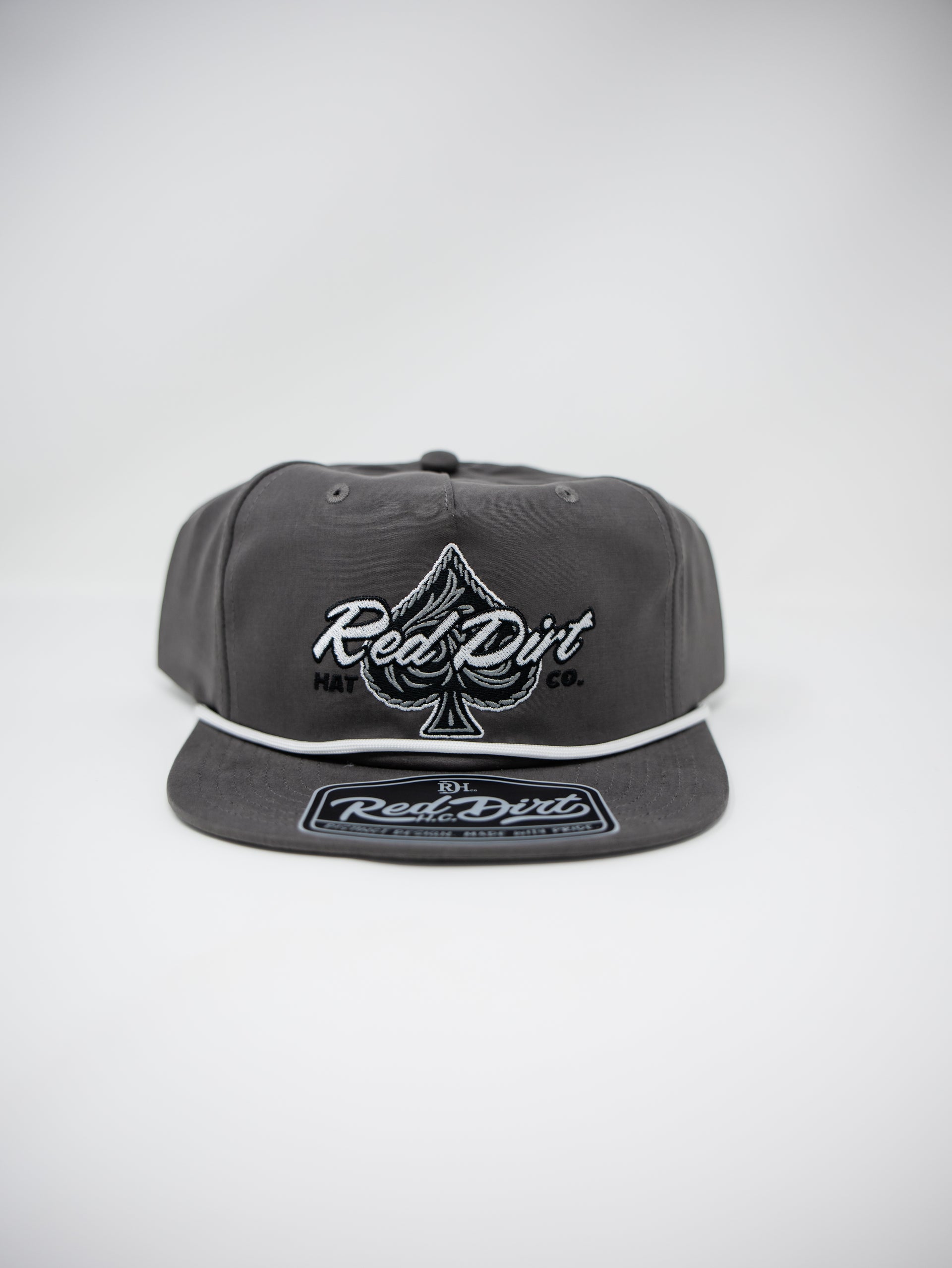 A dark gray snapback cap featuring a white embroidered Red Dirt logo and an ace of spades symbol on the front, with a matching Red Dirt patch on the flat visor, set against a light gray background.