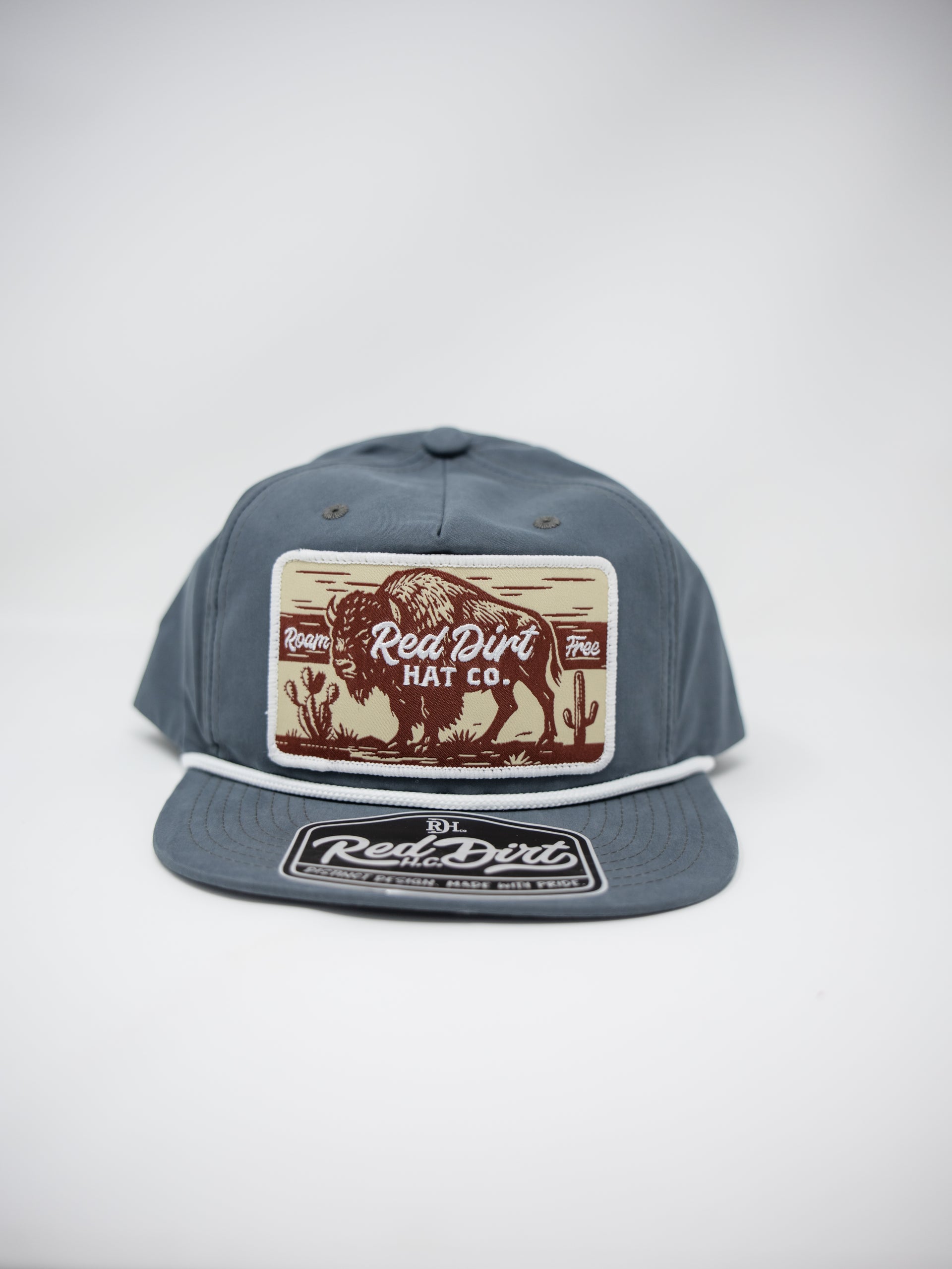 A slate blue snapback cap featuring a rectangular front patch with a bison illustration and the text 'Red Dirt Hat Co.' in brown, along with a matching patch on the flat brim.