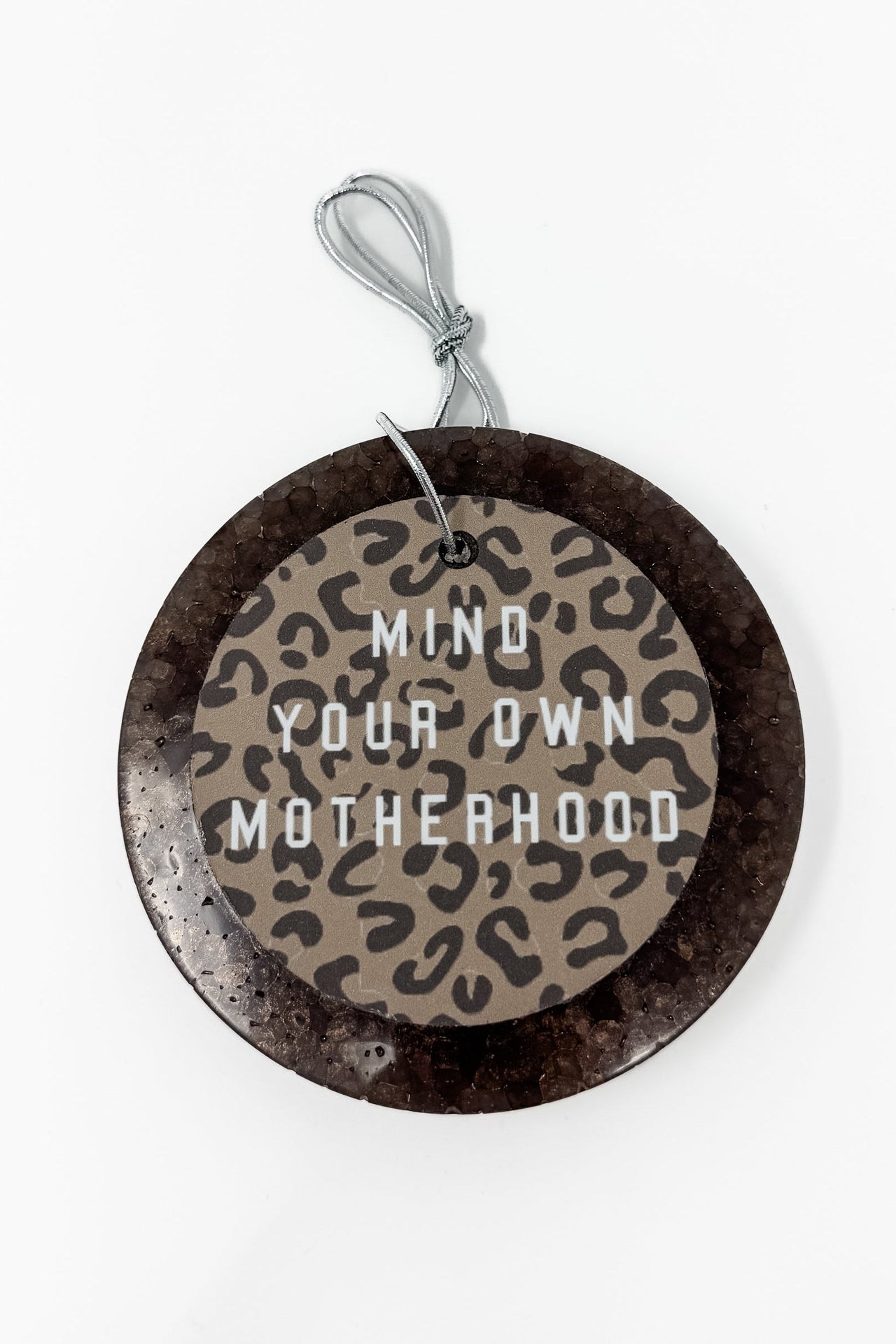 This "Mind Your Own Motherhood" car freshie features a sassy, round design with a bold leopard print center and block lettering, all framed by a smooth, circular outer border. It comes ready to hang from your rearview mirror with an attached silver string. Colors and scents vary.