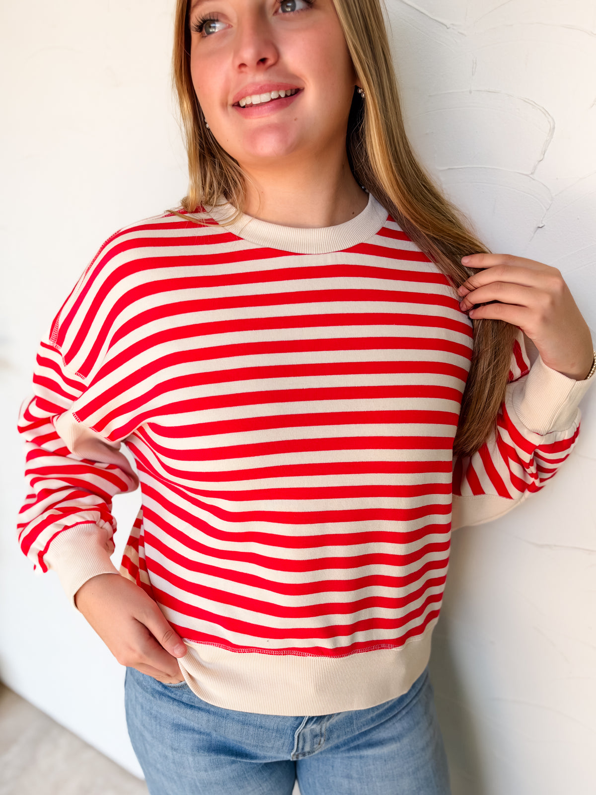 Kenzie wearing the Just Around The Corner Ruby striped oversized sweatshirt by Zenana Premium in size Large, made from 60% cotton and 40% polyester, with red and cream horizontal stripes, solid cream sleeve panels, dropped shoulders, and ribbed trim, styled with light-wash jeans