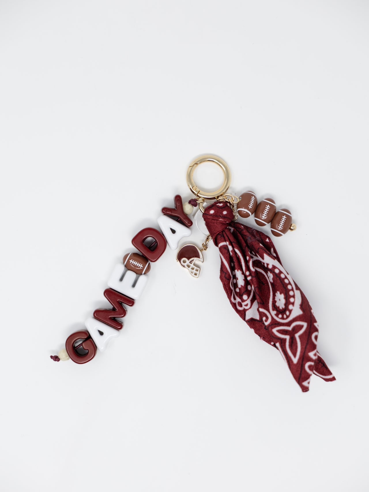 A keychain charm featuring a gold metal split ring, a white and red 'CANDY' beaded bar, a small brown football charm, and a maroon paisley bandana tassel.