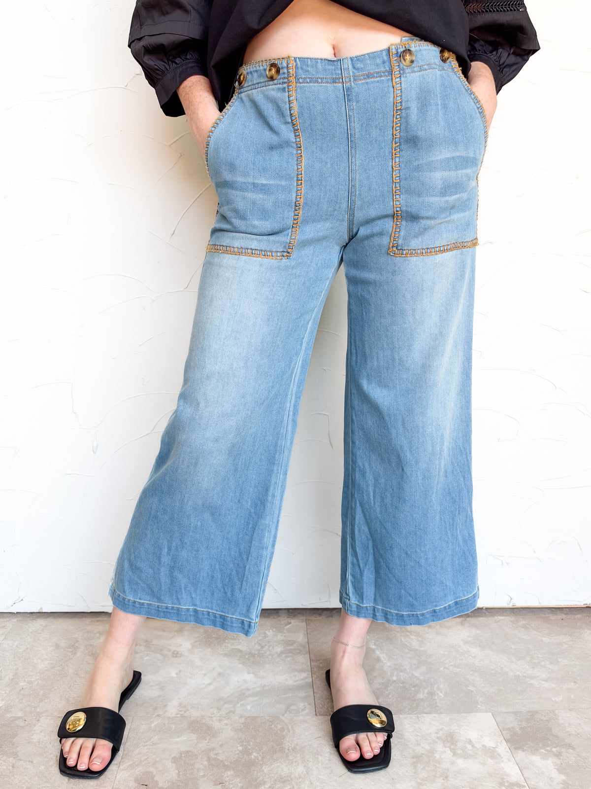 Close-up of eesome Never Let Go Whipstitch Cropped Pants in light blue denim, made from 70% cotton, 28% polyester, and 2% spandex, showing a front patch pocket outlined in golden-tan whipstitch trim.