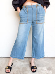Close-up of eesome Never Let Go Whipstitch Cropped Pants in light blue denim, made from 70% cotton, 28% polyester, and 2% spandex, showing a front patch pocket outlined in golden-tan whipstitch trim.