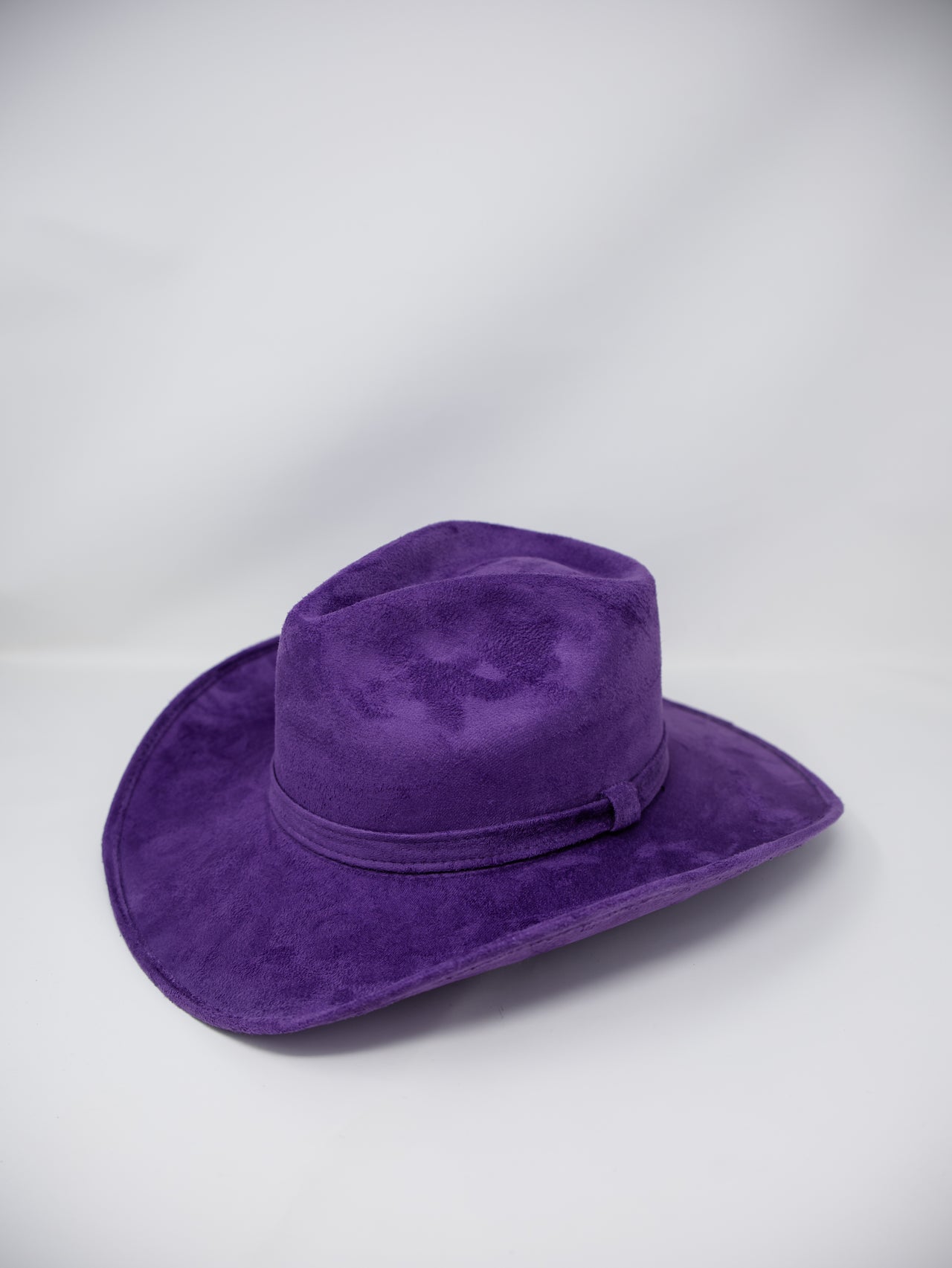 A purple felt cowboy hat with a matching band, photographed on a light gray studio background.