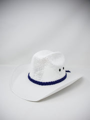 A white woven cowboy hat with a dark blue braided band and small black embroidered eyes, photographed on a light gray studio background.