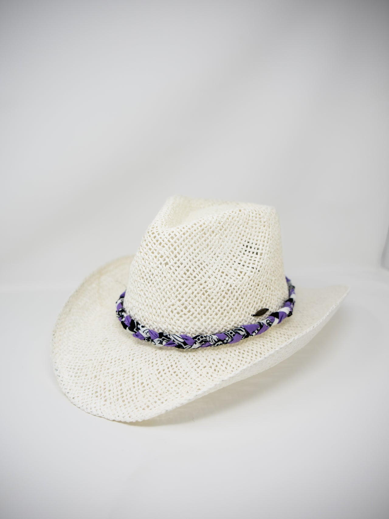 An off-white woven straw cowboy hat featuring a decorative band with purple and black woven details, set against a plain light gray background.