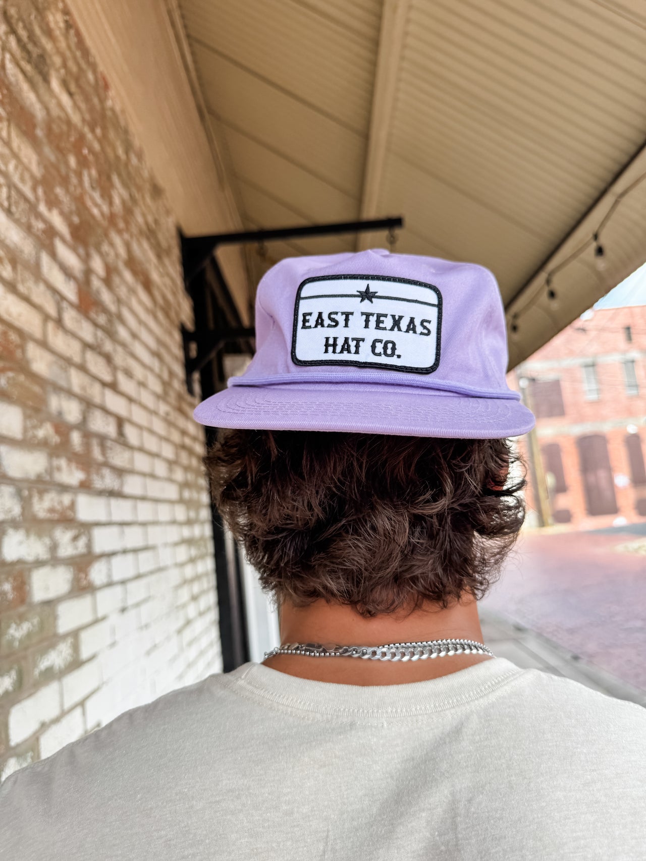 Person wearing a purple cap with 'East Texas Hat Co.' logo, standing outdoors.
