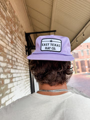 Person wearing a purple cap with 'East Texas Hat Co.' logo, standing outdoors.