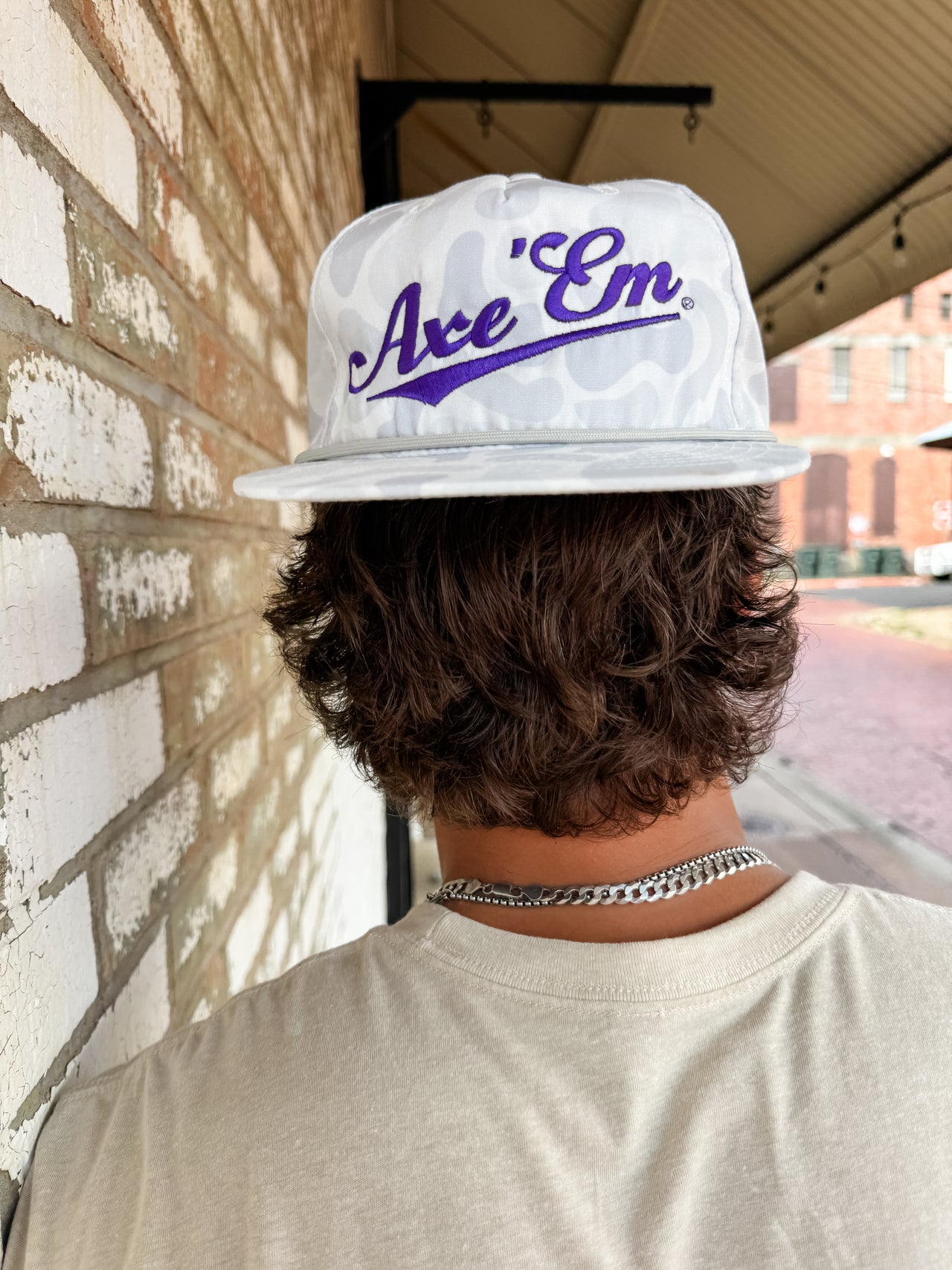 Person wearing a white cap with 'Axe Em' logo against a brick wall.