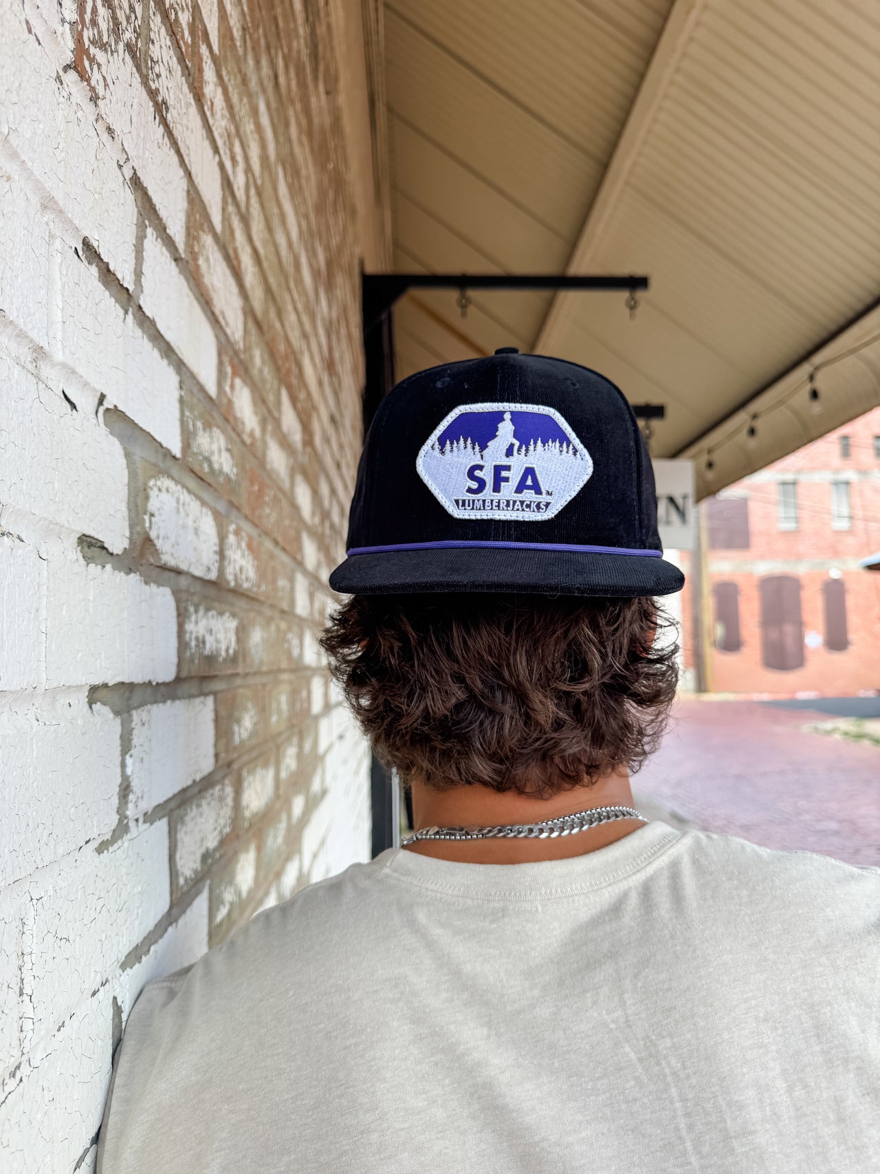 Person wearing a cap with 'SFA' logo against a brick wall and overpass background