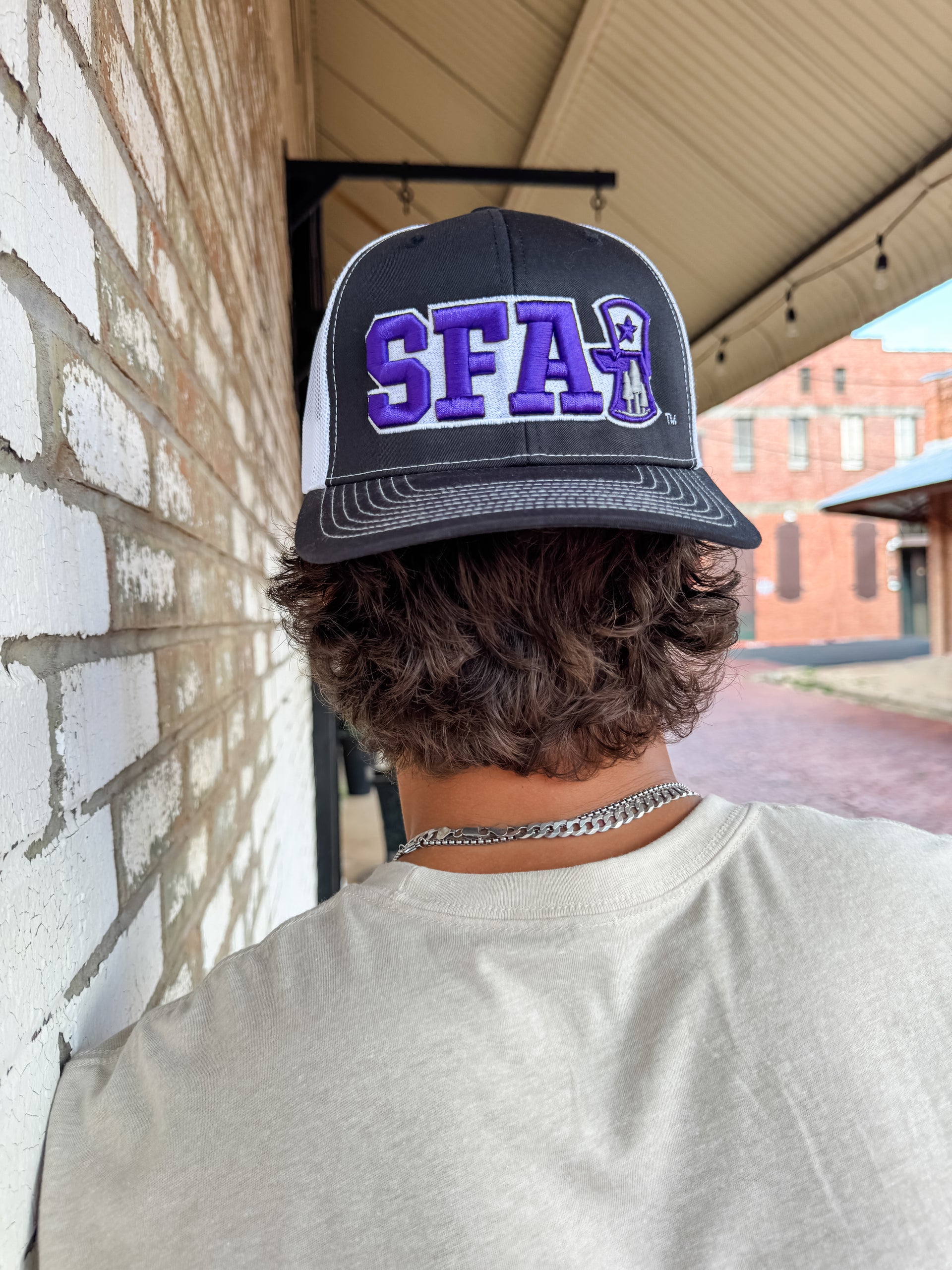 Person wearing a cap with 'SFA' on it, standing against a brick wall.
