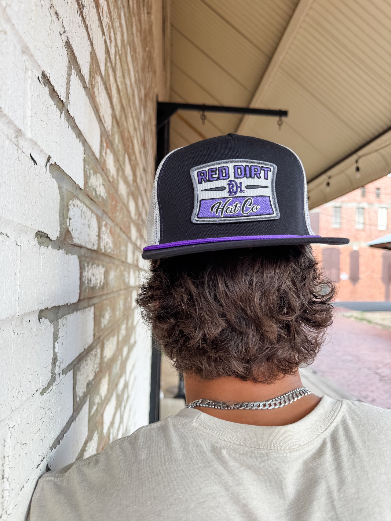Person wearing a cap with 'Red Dirt & Co' logo against a brick wall.