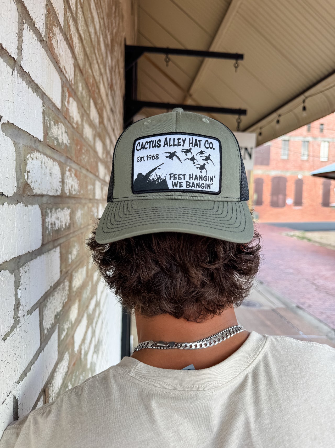 Person wearing a Cactus Alley Hat Co. cap against a brick wall.