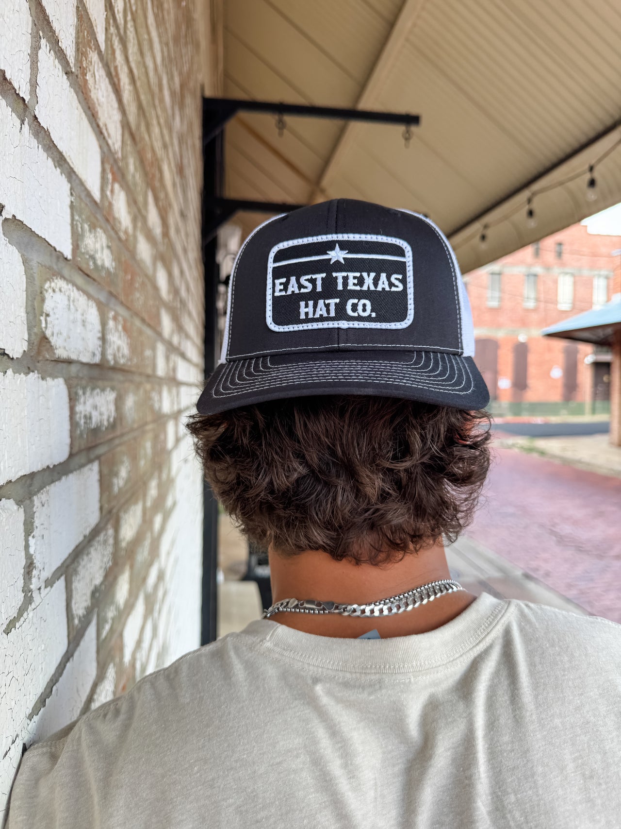 Person wearing a black and white cap with 'East Texas Hat Co.' branding against a brick wall.